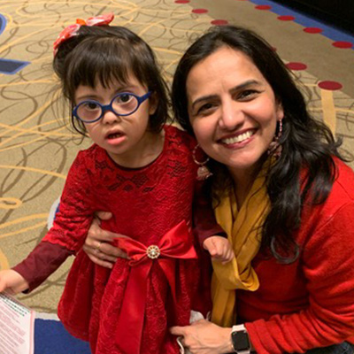 An Indian woman kneeling next to her Indian daughter with Down syndrome looking at the camera and smiling.